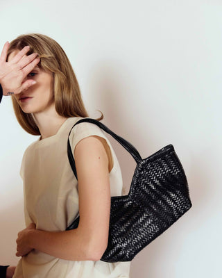 Woman holding a black woven handbag against a plain background
