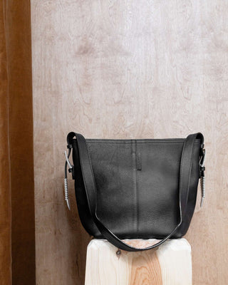 A black leather bag with silver hardware on a wooden pidestal