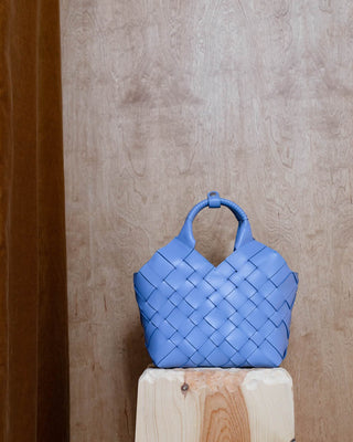A blue woven leather bag on a wooden pidestal