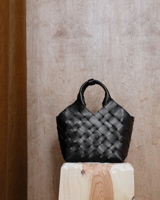 A black woven leather bag on a wooden pidestal