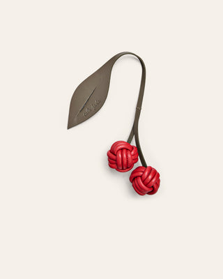 Cala Jade cherry leather bag charm in red and green on a beige background