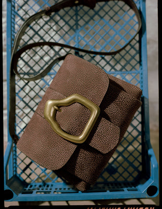 Brown leather handbag with gold buckle on a blue metal crate