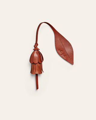 Brown leather bag charm shaped like a flower on a beige background