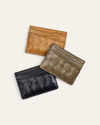 Three woven leather card holders in black, brown, and beige on a light beige background.