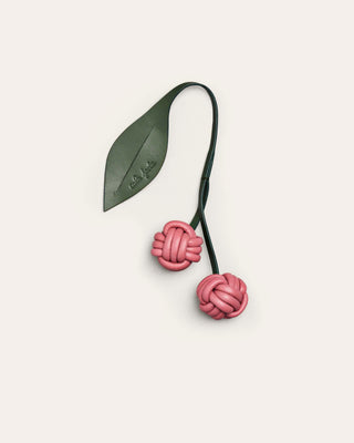 Cherry leather bag charm with a green leaf on a beige background