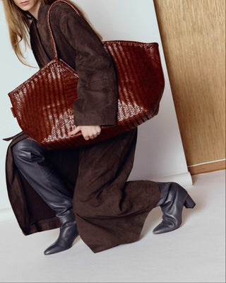 Woman holding a large brown textured bag against a white wall.