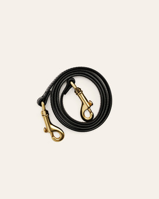 A black leather shoulder strap with brass clasps on a beige background