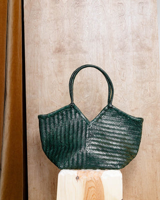 a green woven leather bag on a wooden pidestal