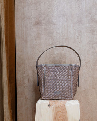 A beige leather bucket bag standing on a wooden pidestal