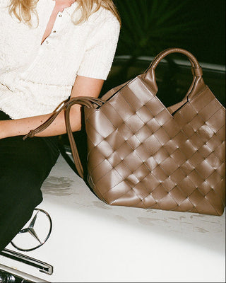 Woman sitting on a car with a brown leather handbag